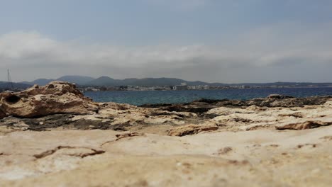 Scenic-close-up-view-of-Ibiza,-Sant-Antoni-rocky-limestone-beach-on-a-warm-sunny-day-with-balearic-sea-an-mountains-in-the-background-in-Spain