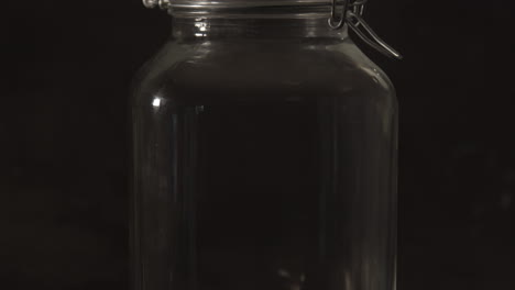 Tilt-up-of-glass-preserving-jar-with-metal-bracket-against-a-black-background