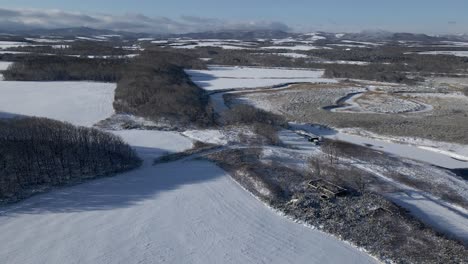 Beautiful-drone-shot-flying-over-snow-covered-fields-in-rural-countryside
