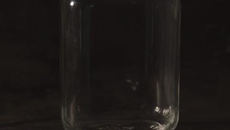Kippen-Sie-Das-Einmachglas-Aus-Glas-Mit-Metallhalterung-Vor-Schwarzem-Hintergrund-Nach-Unten