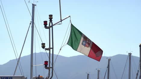 Italian-navy-flag-waving-in-a-breeze-at-the-mast-of-a-ship-in-a-harbour