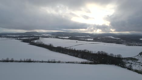Drone-flying-over-fields-and-farmland-in-winter-with-snow-falling