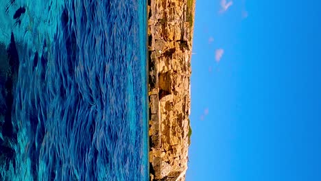 Low-angle-sea-level-view-from-sailing-boat-of-Favignana-island-and-turquoise-sea-water-in-Sicily,-Italy