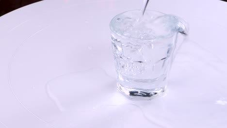 Poruing-water-in-a-transparent-glass-and-overflowing-it