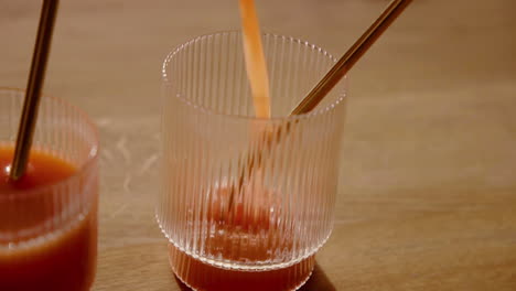 Eine-Kaltgepresste-Orangensaft-Entgiftungsreinigung,-Die-In-Zeitlupe-Mit-Einem-Metallstrohhalm-In-Ein-Trinkglas-Gegossen-Wird