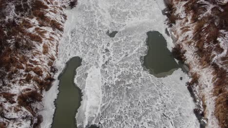 Serene-winter-landscape,-frozen-river-on-cold-day,-aerial-top-down