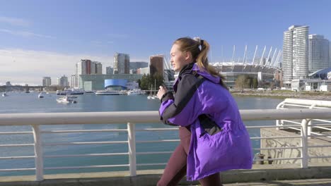 Young-athletic-woman-out-running-by-harbour-wearing-jacket