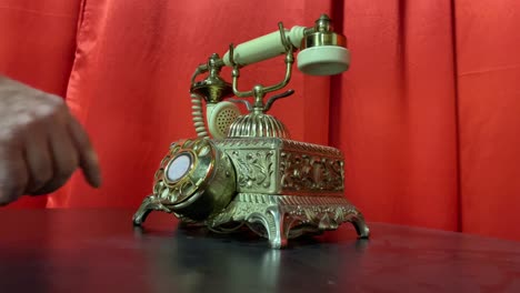 Hand-dialing-old-antique-rotary-telephone-in-gold-with-red-curtain-background