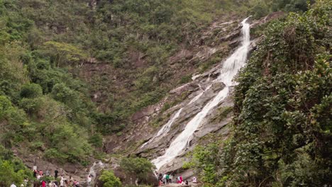 Aerial-view-of-mountain-cascade-waterfall-and-numerous-tourists-gathered-at-the-bottom