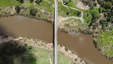 Still-overhead-shot-of-an-old,-historical-bridge-made-of-wooda-and-steel-that-stretches-from-one-land-mass-to-another-over-a-murky-brown-river-on-a-bright-and-warm-day