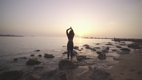 Black-afro-American-young-athletic-woman-practicing-yoga-at-sunrise-on-a-rock-in-the-ocean,-morning-meditative-workout-routine