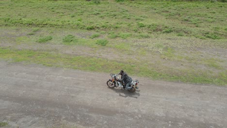 Man-practicing-tricks-on-motorbike-riding-on-dirt-road-in-Africa,-aerial-tracking-shot