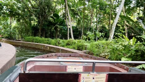 Handheld-shot-of-Amazon-River-Quest-water-ride-at-Singapore-river-wonders,-safari-zoo,-mandai-reserves,-cruising-through-beautiful-lush-green-vegetations-with-sunlight-passing-through-green-foliage