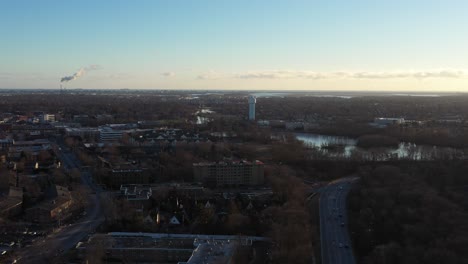 An-aerial-view-over-a-suburban-neighborhood-on-Long-Island-just-before-sunset,-high-enough-to-see-the-horizon,-a-long-road-and-a-lake