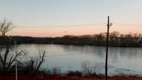 Starting-with-a-low-angle-view-of-a-quiet-lake-surrounded-by-leafless-trees-at-sunset