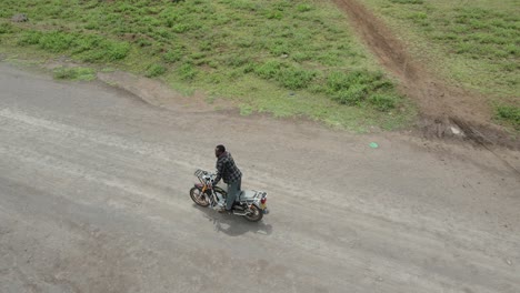 Man-riding-motorcycle-on-dirt-road-in-Africa-performing-stunt,-Loitokitok,-Kenya,-aerial-view