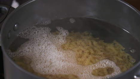 Pouring-a-Bowl-of-Dried-Pasta-in-a-Cooking-Pot-with-Boiling-Water,-Cooking-Fusilli-Pasta-Italian-Noodles