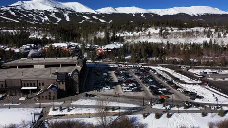 drone-view-of-a-large-number-of-cars-of-different-brands-and-colors-standing-in-a-snowy-parking-lot-with-mountains