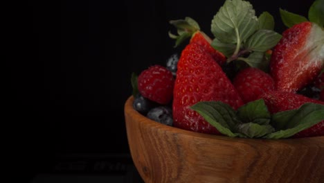 Incredibly-juicy-rotating-forest-fruits-in-a-wooden-bowl-with-black-background,-strawberries,-blueberries,-raspberries,-healthy-fruits,-4K-shot-with-copy-space