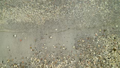Eine-Aufnahme,-Die-Nach-Unten-In-Kieselartigen-Sand-Blickt,-Wobei-Kleine-Wasserschwellungen-Ins-Bild-Kommen
