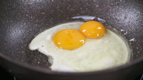 Romper-Y-Freír-Dos-Huevos-En-Una-Sartén-Negra,-Huevos-Fritos,-Yema-De-Huevo-Y-Clara-De-Huevo-Durante-El-Proceso-De-Cocción