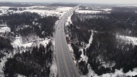 Aerial-Revolving-View-of-4-Lane-Highway-cutting-through-snowy-Rural-landscape-with-frozen-River-Forests-and-Farmland,-Seaton-Trail-Pickering-Ontario