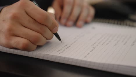 Close-up-of-a-man-writing-on-a-notebook-with-a-black-pen
