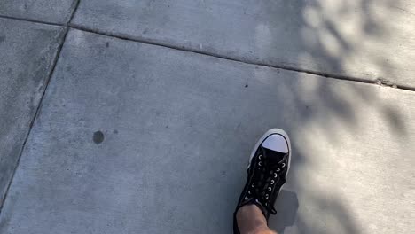 Man-walks-on-sidewalk-wearing-tennis-shoes,-looking-down-POV