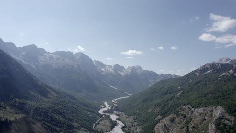 Frontal-drone-video-advancing-over-the-Valbona-valley-and-its-dry-river-at-the-height-of-Llomi,-you-can-see-small-houses-and-a-clear-sky