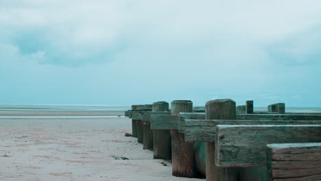 A-small-wooden-structure-stretches-itself-towards-the-ocean-as-the-dried-up-beach-sits-in-silence-at-low-tide-whilst-an-angry-storms-begins-forming-on-the-distant-horizon
