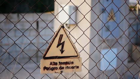 Fenced-off-area-for-protection-against-high-electric-voltage-shock-with-warning-sign-in-Spanish