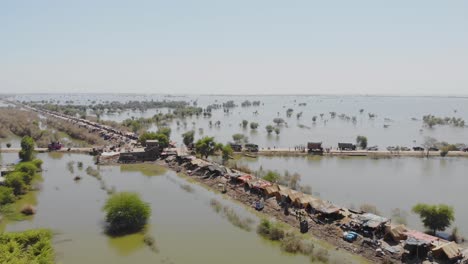Aerial-View-Of-Elevated-Strip-Housing-Makeshift-Tents-Of-Land-Surrounded-By-Flooded-Landscape-In-Jacobabad,-Sindh