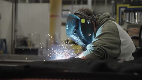 Worker-wearing-face-shield-welding-metal,-bright-sparks-flying-in-workshop