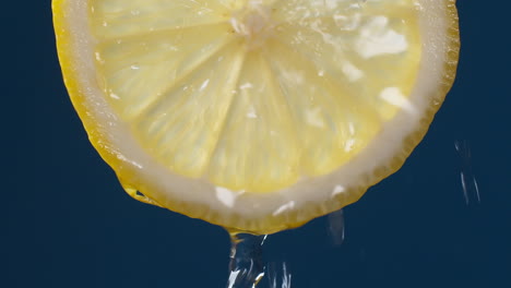 Slow-Motion-Macro-Shot-of-Flowing-Water-from-Lemon-Slice-on-blue-black-Background
