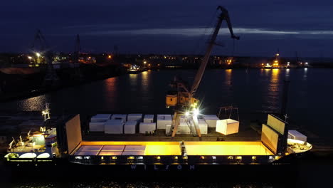 Shipping-containers-being-loaded-on-a-cargo-vessel-at-night-with-a-crane---ascending-aerial-view