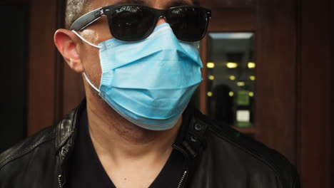 Man-walks-outside,-wearing-covid-19-surgical-mask-and-sunglasses