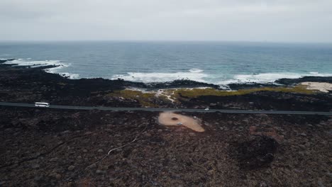 Aerial-view-of-volcanic-coastline,-wavy-ocean-and-straight-road
