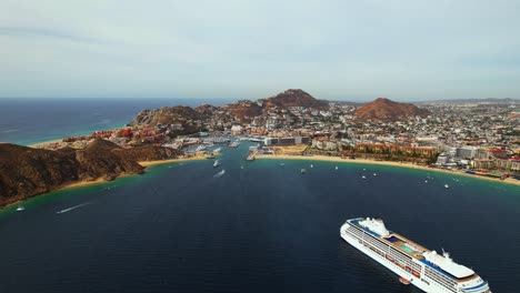 Luftaufnahme-über-Ein-Kreuzfahrtschiff-In-Richtung-Stadtbild-Von-Cabo-San-Lucas,-Mexiko
