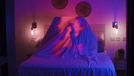 Close-up-shot-of-a-couple-holding-hands-under-a-lit-up-sheet-on-a-bed
