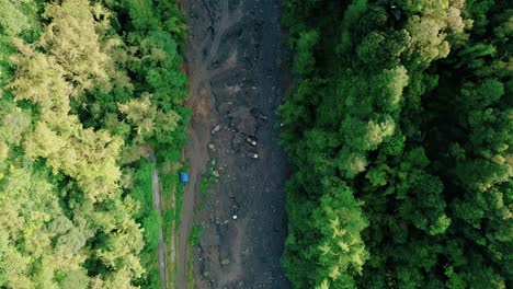 Overhead-Drohne-Filmt-Den-Grund-Eines-Großen-Trockenen-Flusses,-Der-Von-Bäumen-Umgeben-Ist,-Mit-Einem-Lastwagen,-Der-Sandabbauaktivitäten-Durchführt