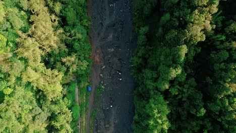 Rocket-drone-footage-of-trucks-at-the-bottom-of-a-large-dry-river-surrounded-by-trees