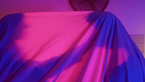 Dolly-shot-of-2-people-under-a-white-sheet-with-a-vibrant-pink-light