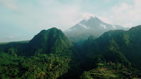 Reveal-drone-shot-of-rain-forest-overgrown-on-the-hill-and-big-valley-with-volcano-on-the-background