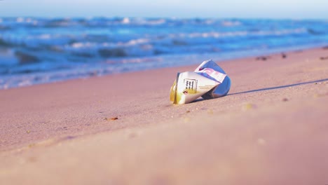 Aluminum-drink-can-on-beach,-trash-and-waste-litter-on-an-empty-Baltic-sea-white-sand-beach,-environmental-pollution-problem,-golden-hour-light-on-evening,-medium-shot