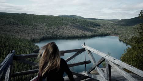 Weiblicher-Kaukasischer-Tourist,-Der-Auf-Einem-Erhöhten-Holzbalkon-Mit-Blick-Auf-Den-Wunderschönen-See-In-Saint-come,-Quebec,-Kanada-Steht
