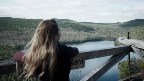 Back-View-Of-Young-Blonde-Woman-Standing-On-Wooden-Observation-Deck,-Enjoying-The-View-Over-Forest-Lake-At-Saint-Come,-Quebec,-Canada
