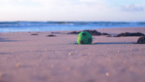 Green-ball-on-the-sand,-trash-and-waste-litter-on-an-empty-Baltic-sea-white-sand-beach,-environmental-pollution-problem,-golden-hour-light-on-evening,-medium-shot