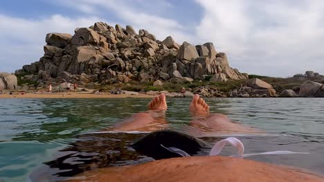 Subjektive-Sicht-Der-Beine-Und-Füße-Des-Mannes,-Die-Sich-Entspannen,-Während-Sie-Auf-Dem-Ruhigen-Meerwasser-Der-Lagune-Von-Lavezzi-Auf-Der-Insel-Korsika-In-Frankreich-Schwimmen
