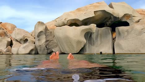 Personal-perspective-of-man-legs-and-feet-relaxing-while-floating-on-calm-sea-water-of-Lavezzi-lagoon-on-Corsica-island-in-France