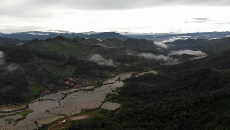 Imágenes-De-Gran-Altitud-De-4k-De-Vuelo-Sobre-Un-Hermoso-Valle-Con-Campos-De-Arroz-En-Un-Valle-Sereno-Cortando-Un-Paisaje-Montañoso-Boscoso-En-Laos,-Sudeste-De-Asia